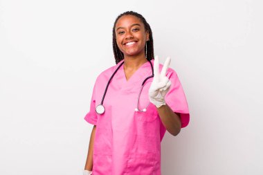 young adult black woman smiling and looking happy, gesturing victory or peace. veterinarian concept