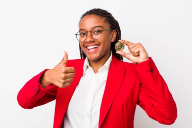 young adult black woman feeling proud,smiling positively with thumbs up. crypto coin concept