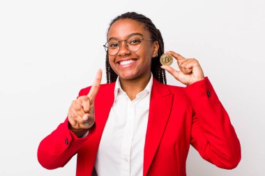 young adult black woman smiling proudly and confidently making number one. crypto coin concept