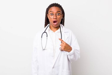 Genç yetişkin siyahi kadın şok olmuş ve ağzı açık, kendini işaret eden bir şekilde şaşırmış görünüyor. hekimlik kavramı