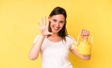 Genç ve güzel bir kadın gülümsüyor ve arkadaş canlısı görünüyor. Beş numarayı gösteriyor. Sıcak kahve ya da çay konsepti
