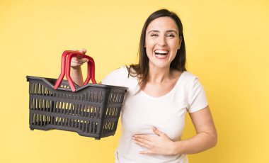 Genç ve güzel bir kadın komik bir şakaya yüksek sesle gülüyor. Alışveriş sepeti konsepti