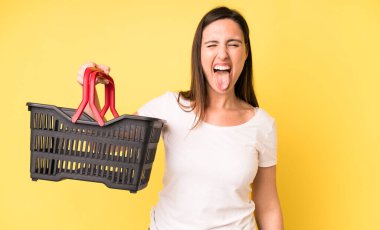 Neşeli ve asi tavırları olan, şaka yapan ve dilini dışarı çıkaran genç ve güzel bir kadın. Alışveriş sepeti konsepti