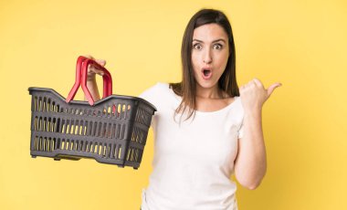 Genç ve güzel bir kadın inançsızlıktan şaşkın şaşkın bakıyor. Alışveriş sepeti konsepti