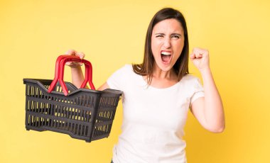 Genç ve güzel bir kadın sinirli bir ifadeyle agresif bir şekilde bağırıyor. Alışveriş sepeti konsepti