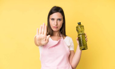 Genç ve güzel bir kadın ciddi görünüyor. Avuç içini gösteriyor. Durdurma hareketi yapıyor. Zeytinyağlı ev aşçısı