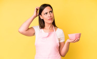 Genç ve güzel bir kadın mutlu bir şekilde gülümsüyor ve hayal kuruyor ya da şüphe ediyor. Ev aşçısı konseptinde yemek pişirmek