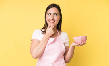 Genç ve güzel bir kadın mutlu, kendinden emin ve elleri çenesinde gülümsüyor. Ev aşçısı konseptinde yemek pişirmek