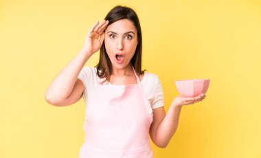 Genç ve güzel bir kadın mutlu, şaşkın ve şaşırmış görünüyor. Ev aşçısı konseptinde yemek pişirmek