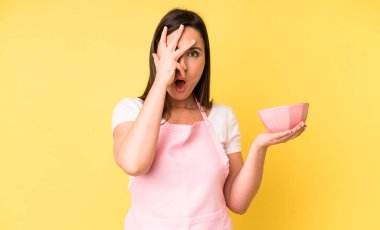 Genç ve güzel bir kadın şok olmuş, korkmuş ya da korkmuş görünüyor. Ev aşçısı konseptinde yemek pişirmek