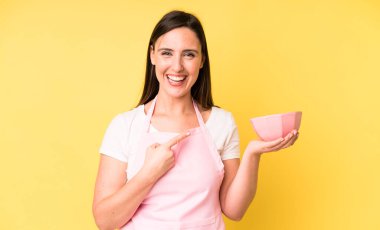 Genç ve güzel bir kadın neşeli bir şekilde gülümsüyor, mutlu hissediyor ve bir tarafı işaret ediyor. Ev aşçısı konseptinde yemek pişirmek