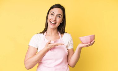 Genç ve güzel bir kadın neşeli bir şekilde gülümsüyor, mutlu hissediyor ve bir konsept gösteriyor. Ev aşçısı konseptinde yemek pişirmek