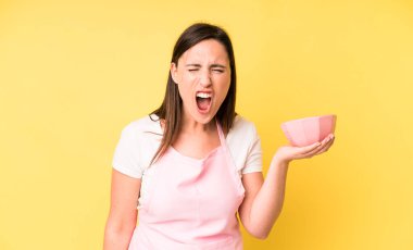 Genç ve güzel bir kadın sinirli bir şekilde bağırıyor. Ev aşçısı konseptinde yemek pişirmek