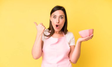 Genç ve güzel bir kadın inançsızlıktan şaşkın şaşkın bakıyor. Ev aşçısı konseptinde yemek pişirmek