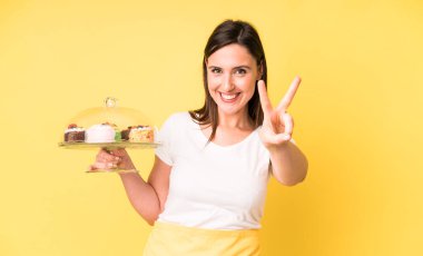 Genç ve güzel bir kadın gülümsüyor ve mutlu görünüyor. Zafer ya da barış işareti yapıyor. Ev yapımı kek konsepti