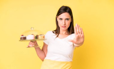 Genç ve güzel bir kadın ciddi görünüyor. Avuç içini gösteriyor. Durdurma hareketi yapıyor. Ev yapımı kek konsepti