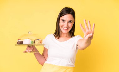 Genç ve güzel bir kadın gülümsüyor ve arkadaş canlısı görünüyor, dört numarayı gösteriyor. Ev yapımı kek konsepti