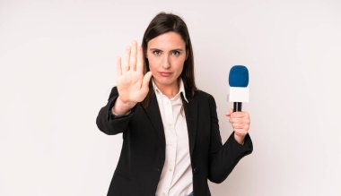 Genç ve güzel bir kadın ciddi görünüyor. Avuç içini gösteriyor. Durdurma hareketi yapıyor. Bir mikrofon konseptine sahip sunucu