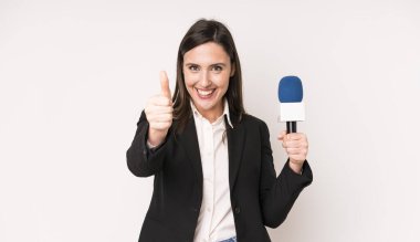 Genç ve güzel bir kadın gururlu, olumlu gülümsüyor. Bir mikrofon konseptine sahip sunucu