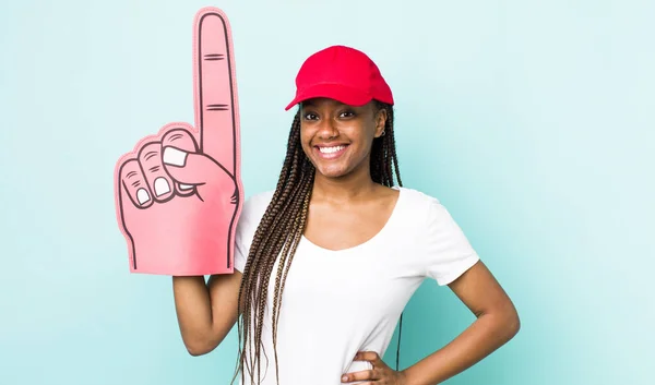 young adult black woman smiling happily with a hand on hip and confident. number one hand fan concept