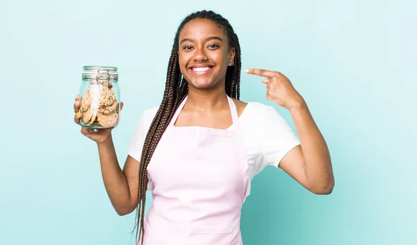 young adult black woman smiling confidently pointing to own broad smile. home made cookies concept