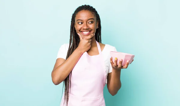 young adult black woman smiling with a happy, confident expression with hand on chin. empty bowl concept