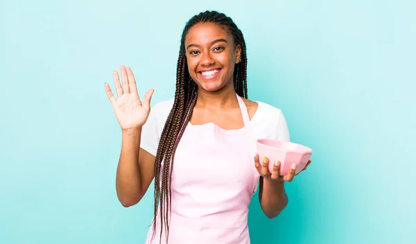 young adult black woman smiling happily, waving hand, welcoming and greeting you. empty bowl concept