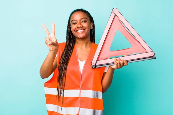 young adult black woman smiling and looking happy, gesturing victory or peace. car emergency triangle concept