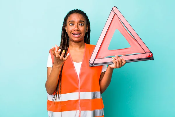 young adult black woman looking desperate, frustrated and stressed. car emergency triangle concept