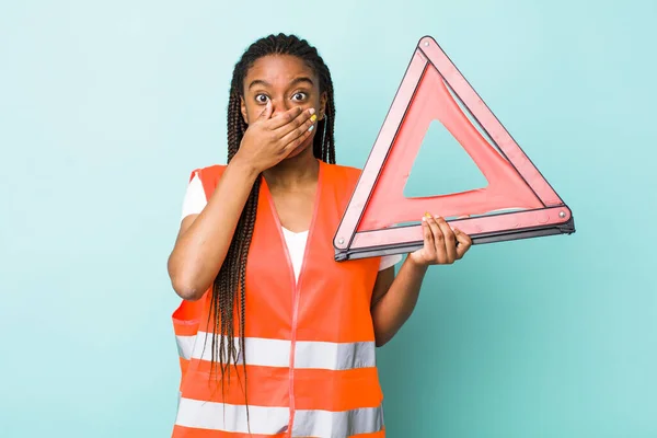young adult black woman covering mouth with hands with a shocked. car emergency triangle concept