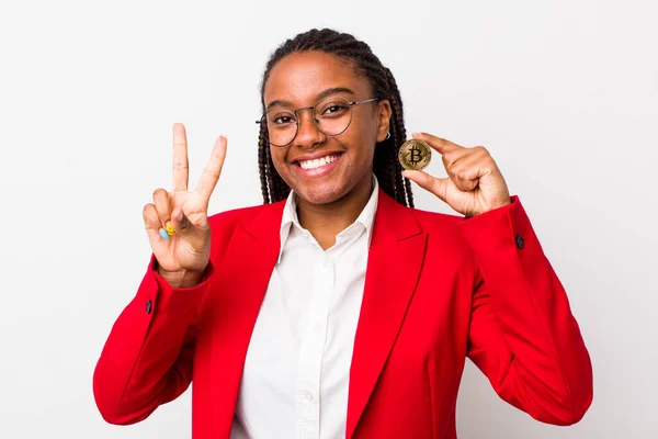 young adult black woman smiling and looking happy, gesturing victory or peace. crypto coin concept