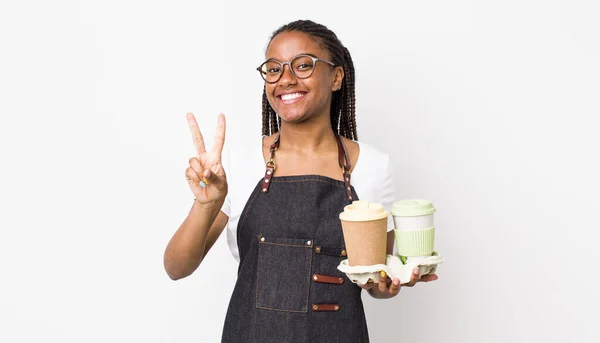 young adult black woman smiling and looking happy, gesturing victory or peace. take away coffees concept