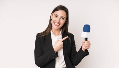 Genç ve güzel bir kadın neşeli bir şekilde gülümsüyor, mutlu hissediyor ve bir tarafı işaret ediyor. Bir mikrofon konseptine sahip sunucu