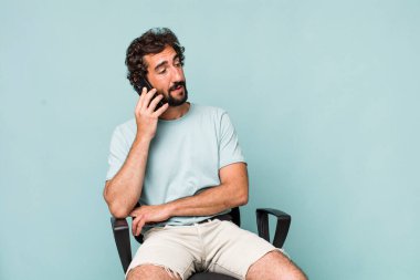 Genç, Latin asıllı, deli bir adam sandalyeye oturmuş telefonunu kullanıyor.