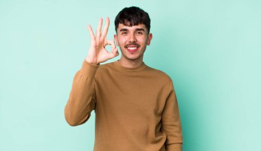 Genç, İspanyol bir adam mutlu, rahat ve tatmin olmuş hissediyor. Onayını iyi bir hareketle gösteriyor. Gülümsüyor.