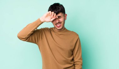 Genç, Latin bir adam stresli, yorgun ve hayal kırıklığına uğramış görünüyor. Alnından ter akıyor. Umutsuz ve bitkin hissediyor.