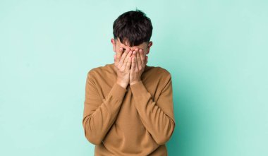 Genç, Latin bir adam üzgün, hayal kırıklığına uğramış, gergin ve depresif hissediyor. İki eliyle yüzünü kapatıyor, ağlıyor.