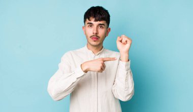 Genç, İspanyol asıllı, sabırsız ve sinirli bir adam, saati gösteriyor, dakiklik istiyor, dakik olmak istiyor.