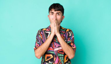 Genç, Latin bir adam endişeli, üzgün ve korkmuş hissediyor. Ağzını ellerle kapatıyor. Endişeli ve berbat görünüyor.