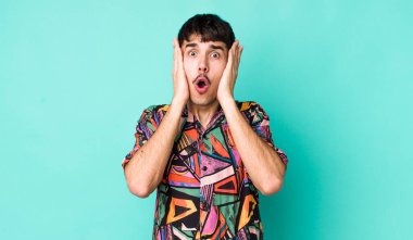 Genç, Latin asıllı bir adam hoş olmayan bir şekilde şok olmuş, korkmuş ya da endişeli görünüyor ağzı sonuna kadar açık ve iki kulağını da elleriyle kapatıyor.