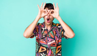 Genç, İspanyol bir adam şok olmuş, şaşırmış ve şaşırmış hissediyor. Elinde şaşkın, inançsız bir bakışla gözlük tutuyor.