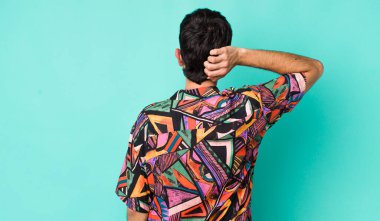 Genç, Latin asıllı, bilgisiz ve kafası karışık bir adam, bir çözüm düşünüyor, eli kalçasında, diğeri kafasında, dikiz aynasından.