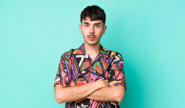 Genç, Latin asıllı bir adam hayal kırıklığına uğramış ve hayal kırıklığına uğramış hissediyor. Ciddi görünüyor, kızgın ve kollarını kavuşturmuş.