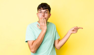 Genç, Latin bir adam mutlu, şaşkın ve şaşırmış hissediyor. Ağzını eliyle kapatıyor ve yanal fotokopi alanını işaret ediyor.