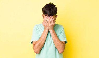 Genç, Latin bir adam üzgün, hayal kırıklığına uğramış, gergin ve depresif hissediyor. İki eliyle yüzünü kapatıyor, ağlıyor.