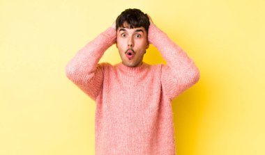 Genç, Latin asıllı bir adam heyecanlı ve şaşırmış görünüyor, ağzı açık, iki eli başında, kendini şanslı bir kazanan gibi hissediyor.