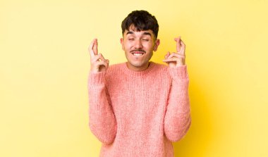 Genç, Latin asıllı, gülümseyen ve endişeyle iki parmağını çaprazlayan endişeli ve iyi şanslar dileyen genç bir adam.