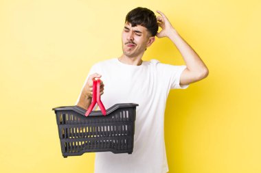 Genç İspanyol adam mutlu bir şekilde gülümsüyor ve hayal kuruyor ya da şüphe ediyor. boş alışveriş sepeti kavramı