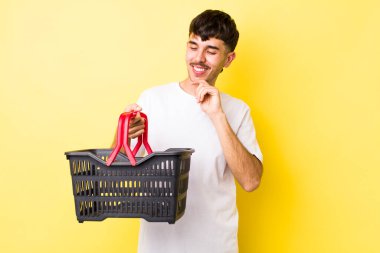 Mutlu, kendinden emin, elleri çenesinde gülümseyen genç bir İspanyol. boş alışveriş sepeti kavramı