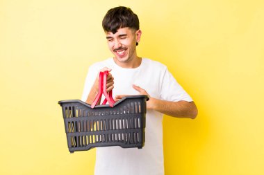 Genç İspanyol bir adam komik bir şakaya yüksek sesle gülüyor. boş alışveriş sepeti kavramı